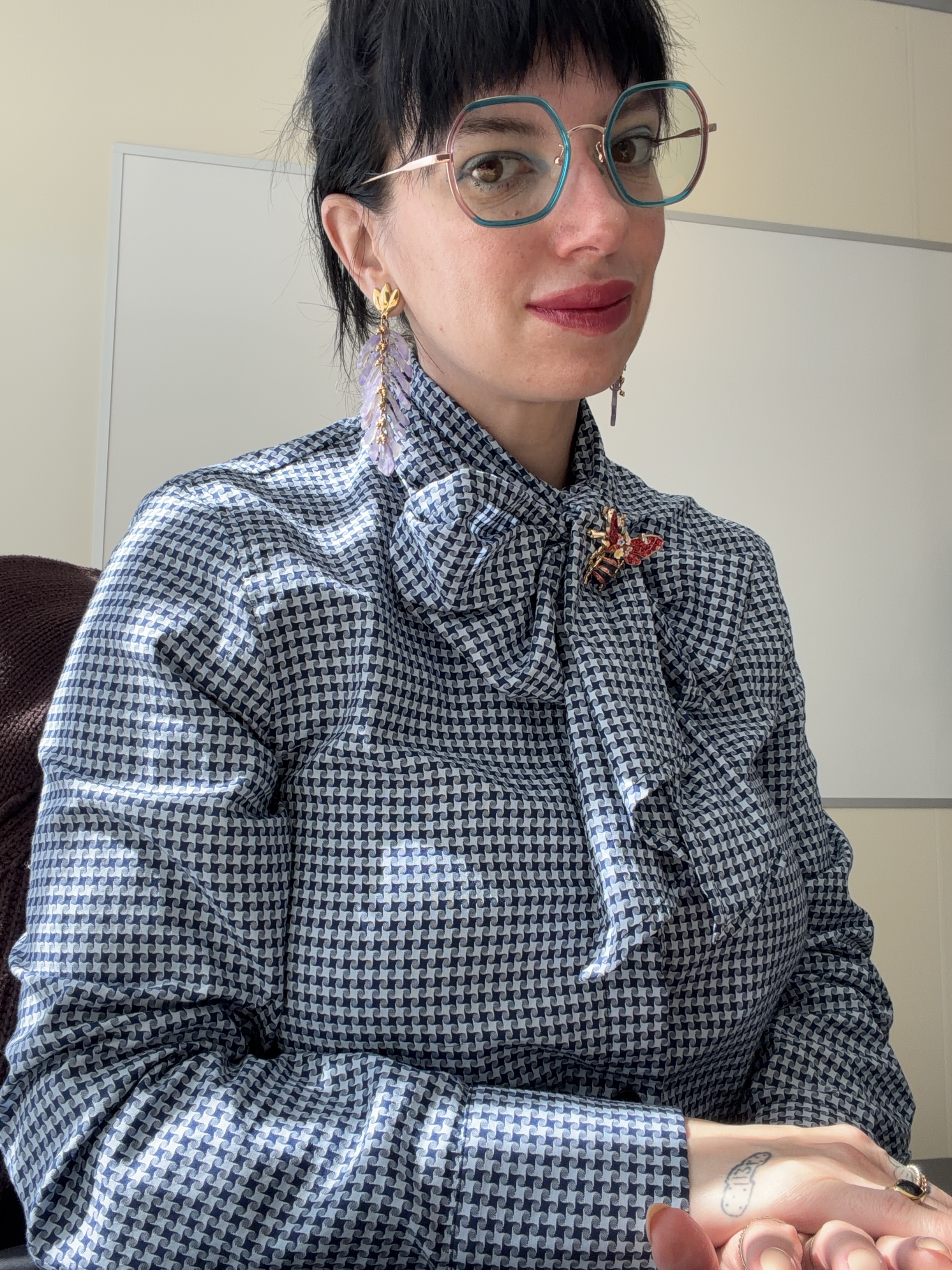 Misha wearing colorful glasses, lavender earrings, and a patterned blouse